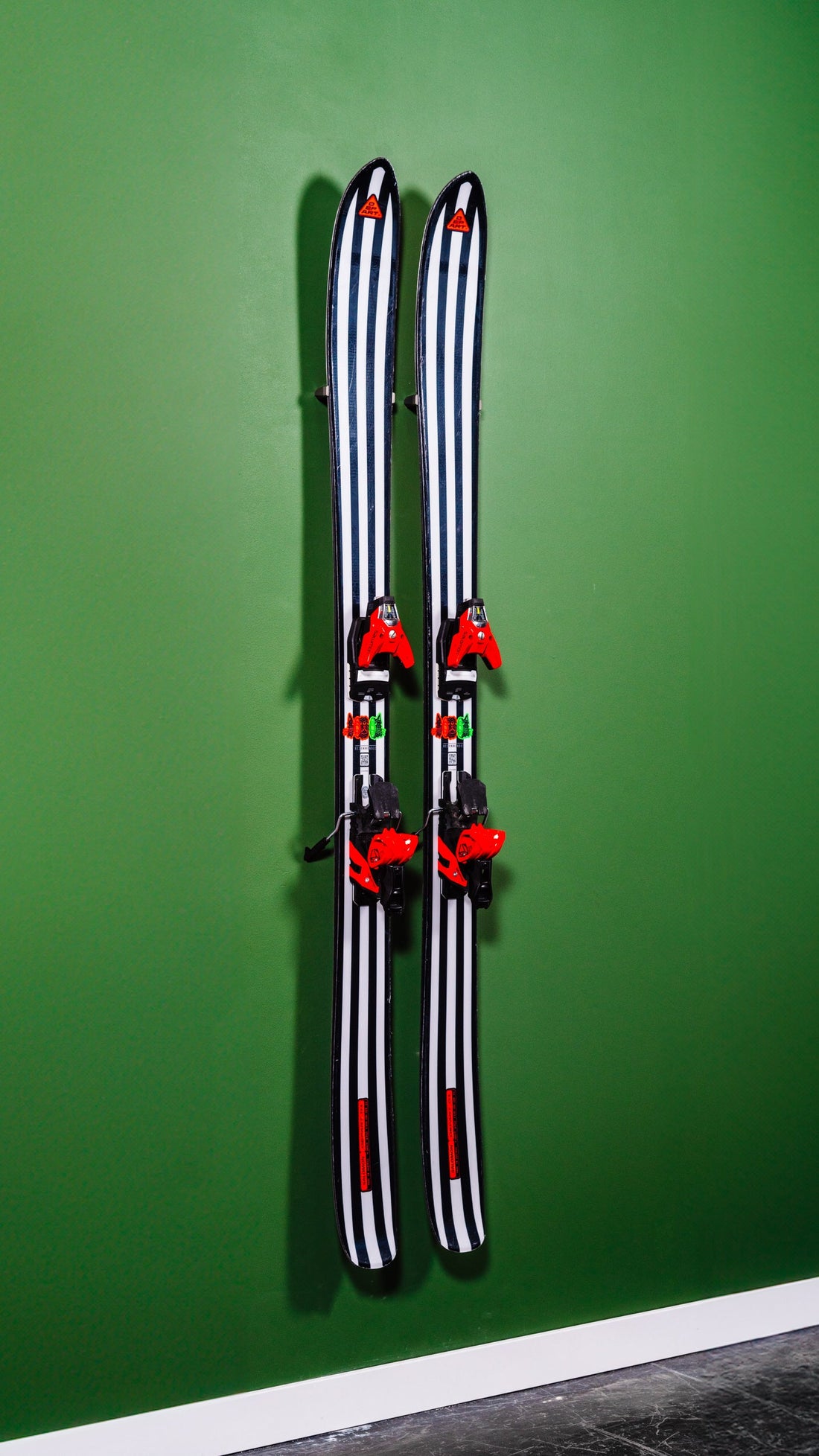 Black and White Striped Skis with Red Bindings on Bold Green Wall: A Modern Alpine Display